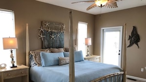 Una cama con dosel y un edredón azul, decoración de paredes con forma de estrella de mar y un ventilador de techo.