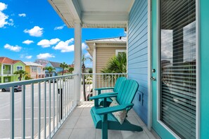 A balcony with teal chairs, a white railing, and a view of neighboring houses.