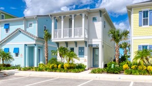A row of coastal-style buildings with balconies, palm trees, and a clear sky.