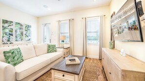 A living room with a beige sofa, a coffee table, and a TV mounted on the wall.