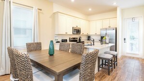 A modern kitchen with white cabinets, stainless steel appliances, and a wooden dining table with woven chairs.