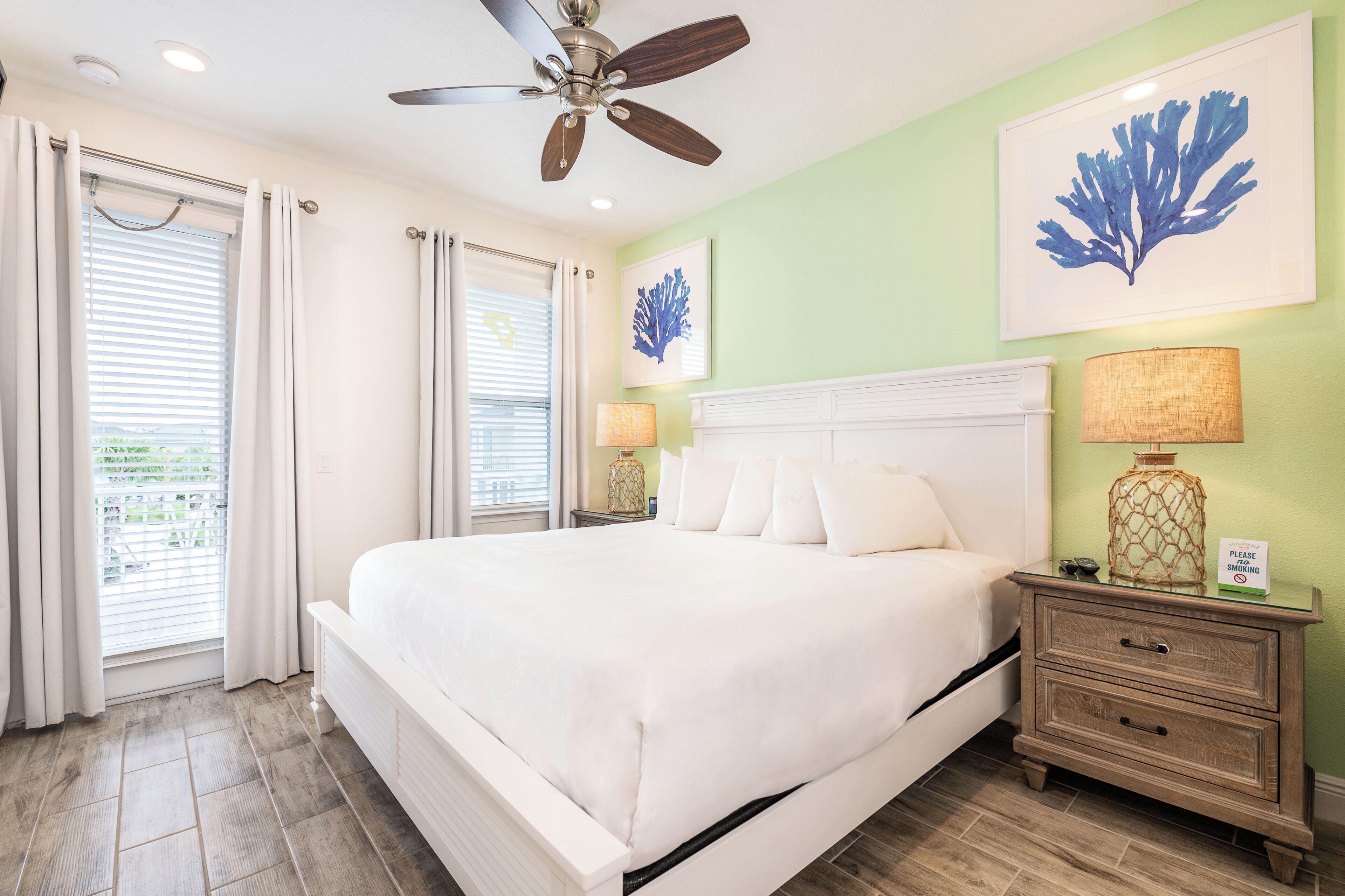 A bedroom with a bed, a nightstand, a ceiling fan, and artwork on the wall.