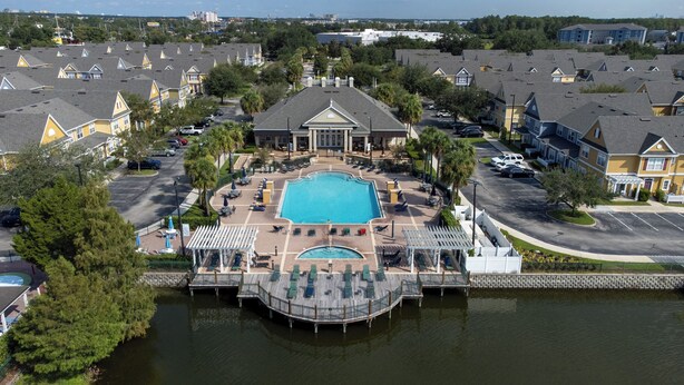 A large swimming pool surrounded by lounge chairs and a deck extending over water, with a building in the background. - Hot tub!! Family Friendly - Loving Home (Kissimmee)