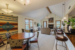 A spacious living area with a wooden dining table, bar stools, and a fireplace.