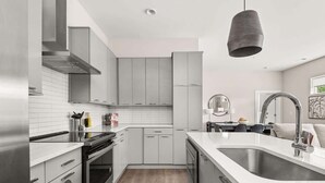 Una cocina moderna con armarios grises, electrodomésticos de acero inoxidable, encimera blanca y una lámpara colgante.