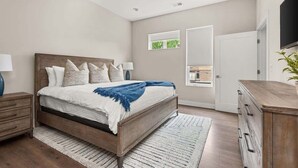 Un dormitorio con cama, mesitas de noche, ventilador de techo, ventana y televisor.