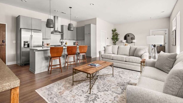 Una cocina moderna con electrodomésticos de acero inoxidable, una zona de comedor con sillas de madera, una sala de estar con sofá y mesa de centro, y una alfombra estampada.