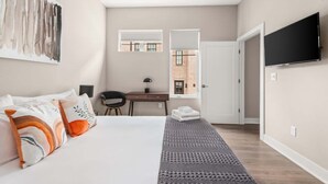 A hotel room with a bed, a desk, a television, and a view of a brick building.