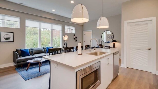 A modern kitchen with a central island, pendant lights, and a dining area with a sofa and chairs.