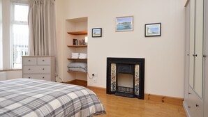 Ein Schlafzimmer mit einem Bett, einem Kamin, Regalen mit Büchern und gerahmten Bildern an der Wand.