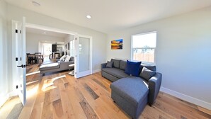 A spacious living area with a grey sectional sofa, a wooden floor, and a large window providing natural light. - Family Retreat in The Village - Yard & Patio (Arroyo Grande)