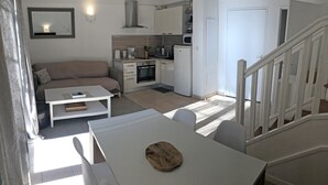 Un espace de vie compact comprenant un coin cuisine, un canapé, une table à manger et un escalier.