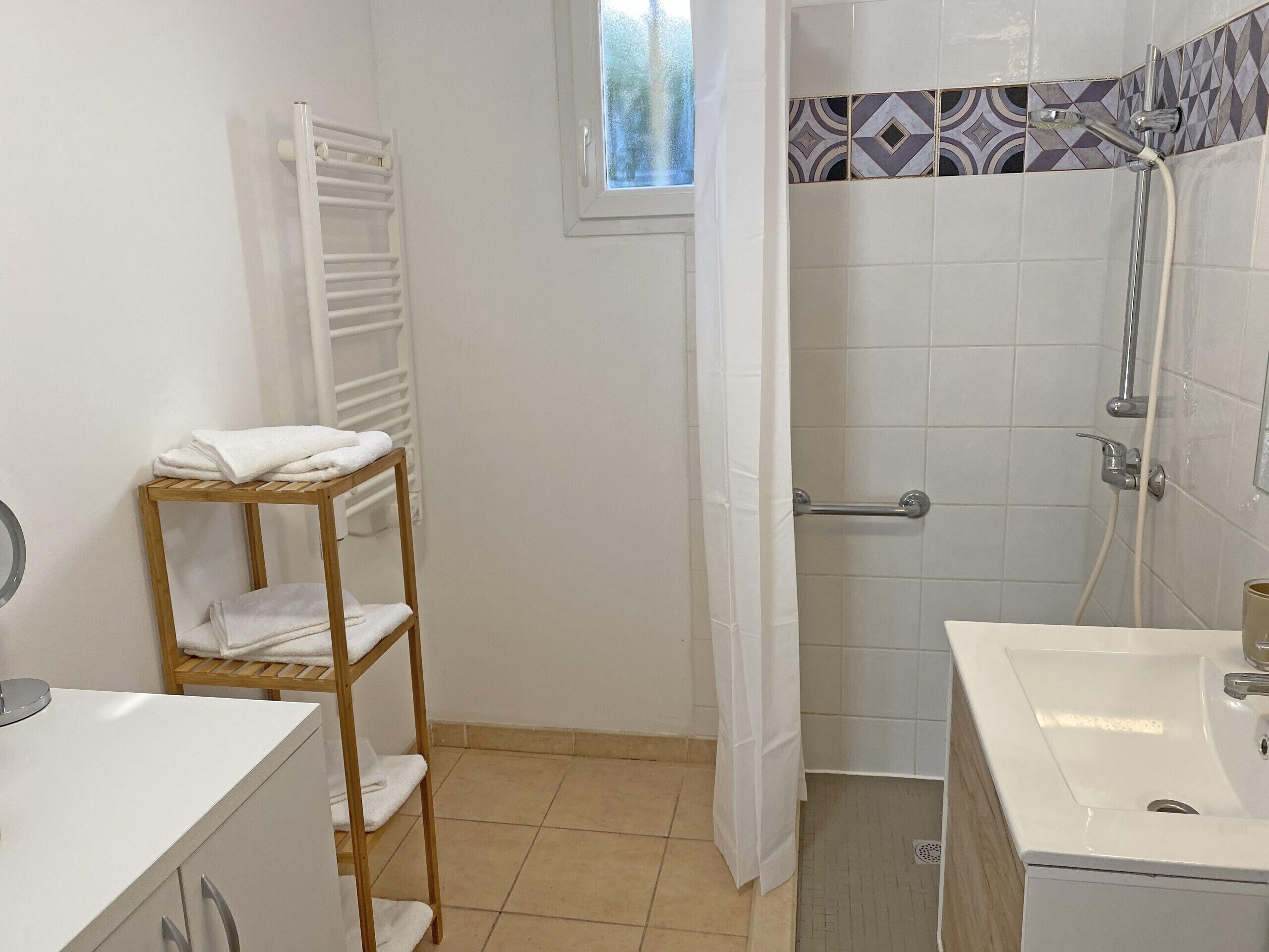 A bathroom with a shower, a sink, a towel rack, and a window.