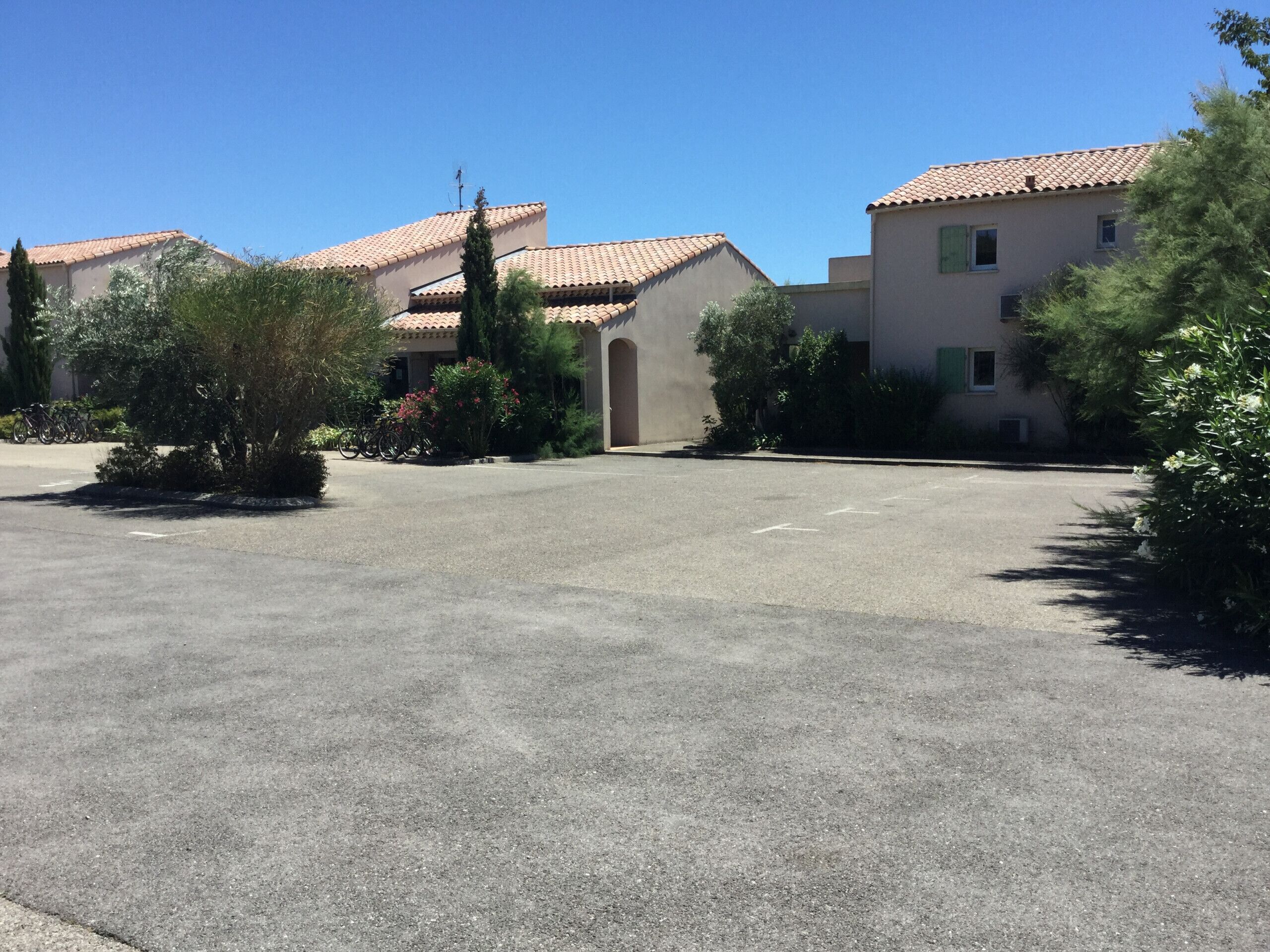 A residential area with two houses, a paved driveway, and surrounding greenery.