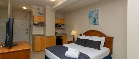 A hotel room with a bed, a desk, a television, a kitchenette, and a painting on the wall.