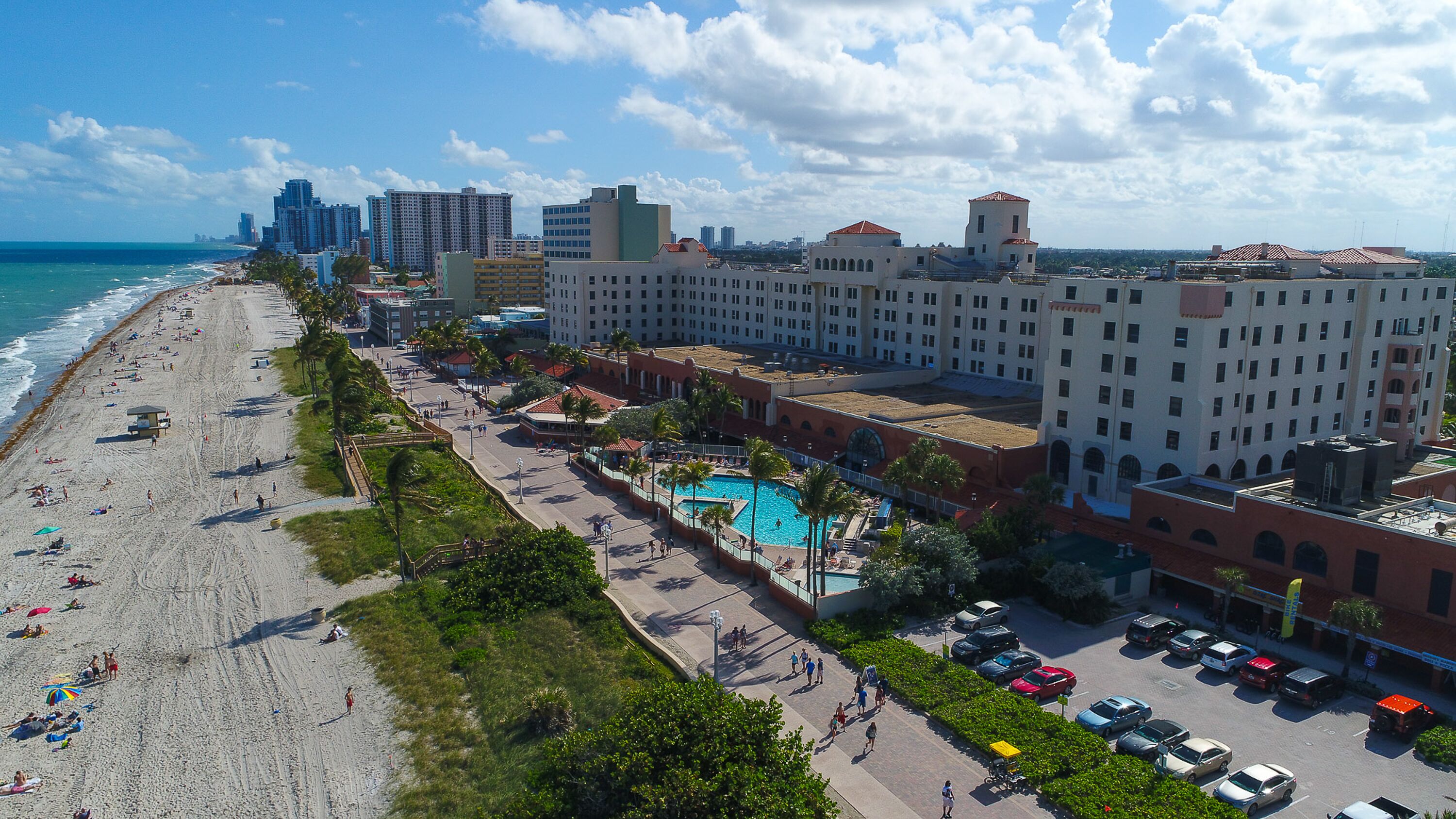 A coastal hotel with a swimming pool, beach access, and a parking area.