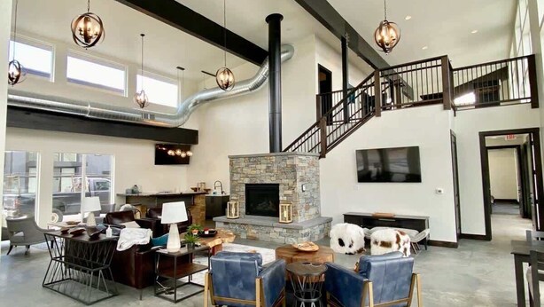A spacious living area with a stone fireplace, modern furniture, and a staircase.