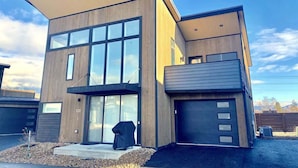 A modern two-story house with a garage, large windows, and a covered outdoor area.
