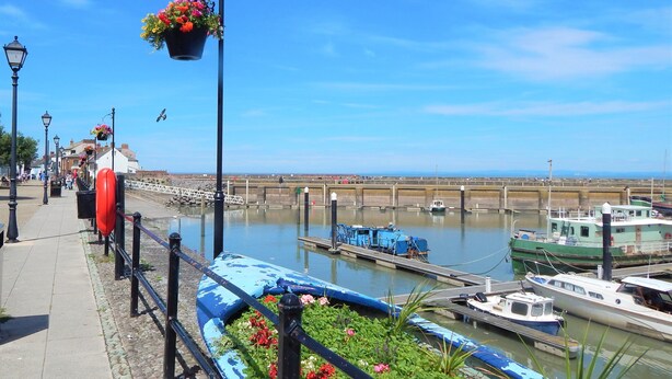 Eine Uferpromenade mit einem Kanal, Booten und einer Brücke im Hintergrund.