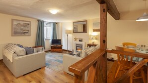 Ein Wohnzimmer mit Sofa, Fernseher, Kamin und Essbereich mit Holzmöbeln.
