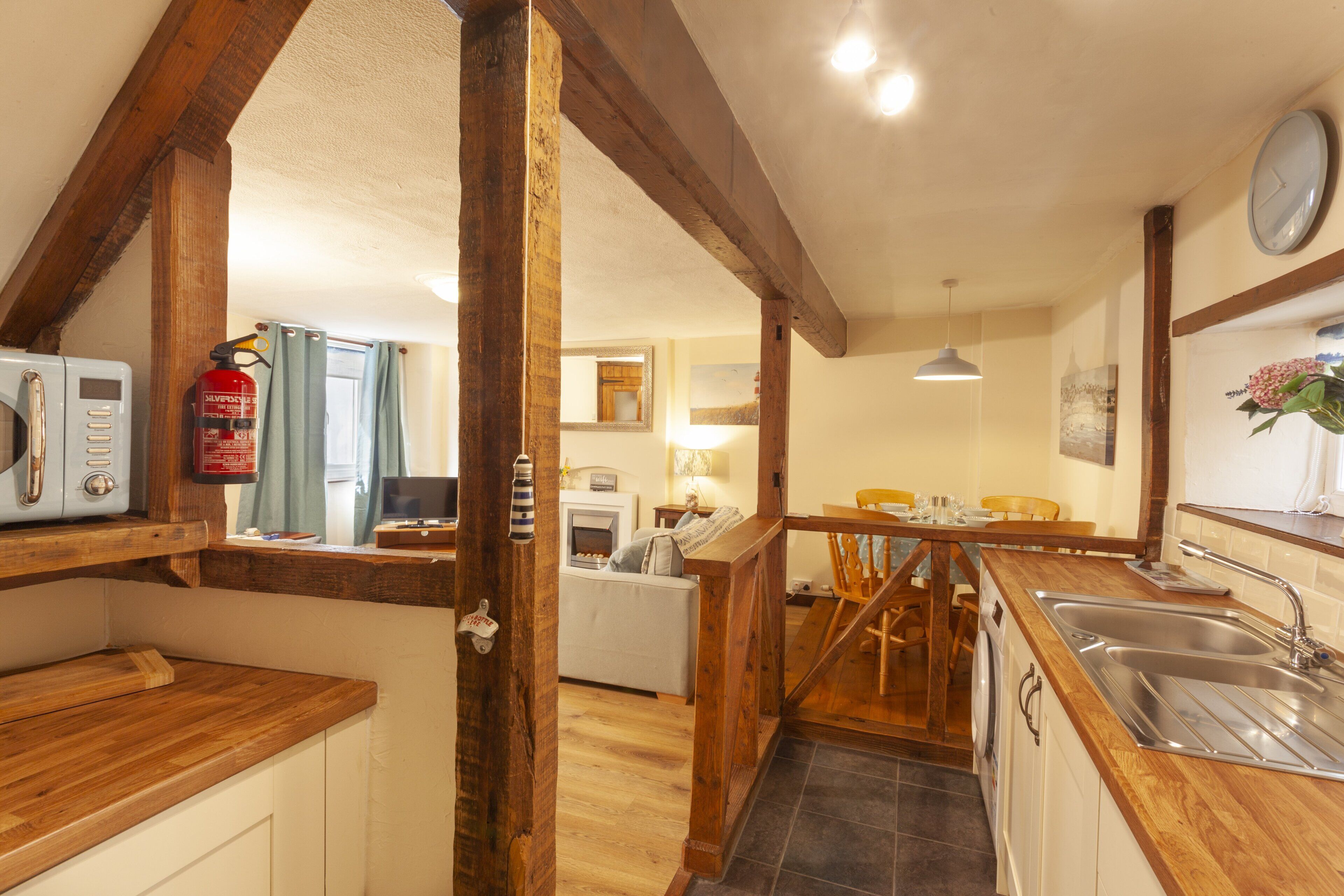 A kitchen with wooden beams, a microwave, a fire extinguisher, a dining area with chairs, and a sink.