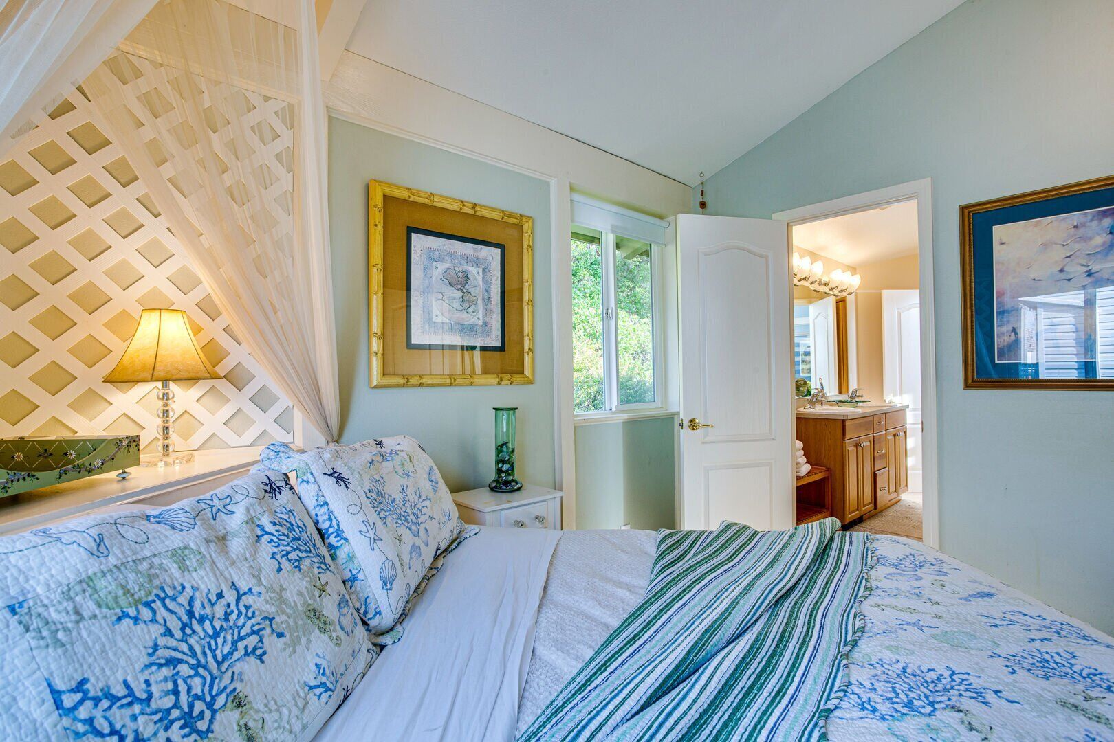 A bedroom with a bed, a nightstand, a lamp, a framed picture, and a door leading to a bathroom.