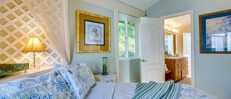 A bedroom with a bed, a nightstand, a lamp, a framed picture, and a door leading to a bathroom.