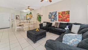 A living room with a black sofa, ottoman, and ceiling fans. There is a dining area with a table and chairs.