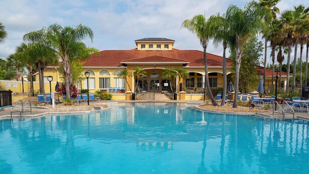 A swimming pool with a building in the background, palm trees, and a clear sky.