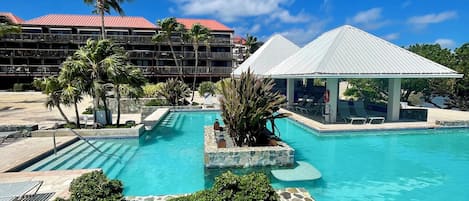 A resort pool area with a clear blue sky, palm trees, and a building with a red roof.