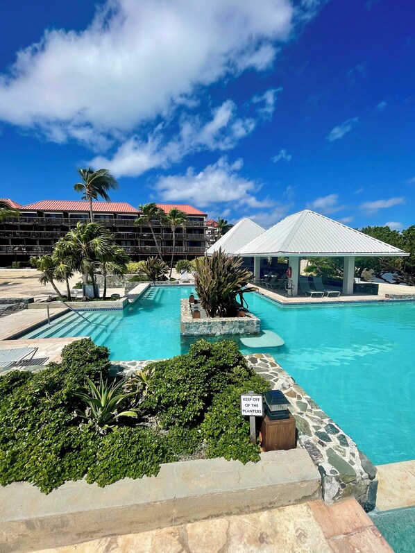 A resort pool area with a clear blue sky, palm trees, and a building with a red roof.