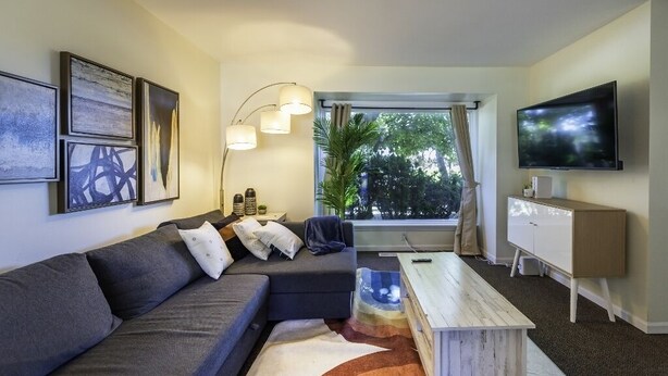 A modern living room with a sectional sofa, a flat-screen TV, a coffee table, and artwork on the walls. - Homey 3BR/2.5BA Townhouse, Walk to Big House! (Ann Arbor)