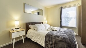 A hotel room with a bed, bedside lamps, a nightstand, a mirror, and a window with curtains. - Homey 3BR/2.5BA Townhouse, Walk to Big House! (Ann Arbor)