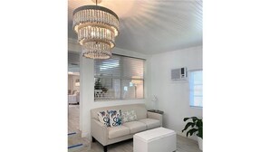A modern living room with a beige sofa, a white ottoman, and a large chandelier.