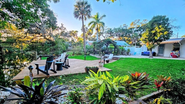 A backyard with a wooden deck, outdoor seating, a small pond, and various plants. - Our Cottage is on Whitaker Bayou minutes from Sarasota Main St. downtown (Sarasota)