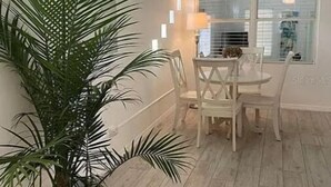 A dining area with a white table and chairs, a ceiling fan, and a large potted plant.