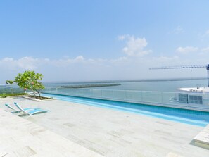A rooftop infinity pool with clear views of the ocean and a distant bridge.