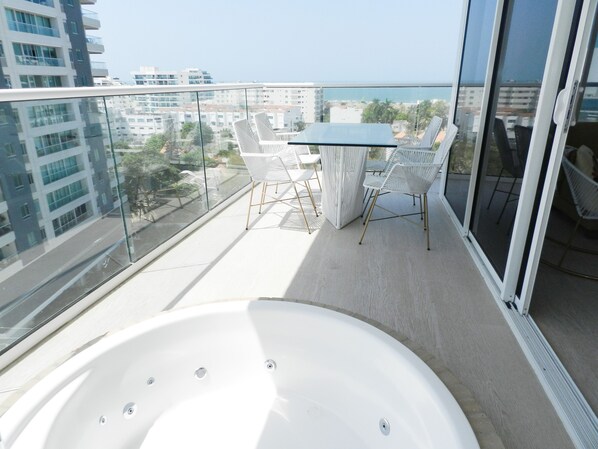 A balcony with a white hot tub, white chairs, and a glass table.