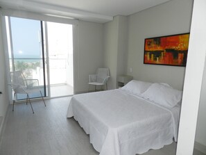 A bedroom with a bed, a chair, a painting, and a balcony with a view.