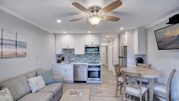 A modern kitchen with white cabinets, a built-in oven, and a microwave. There is a dining area with a round table and chairs.