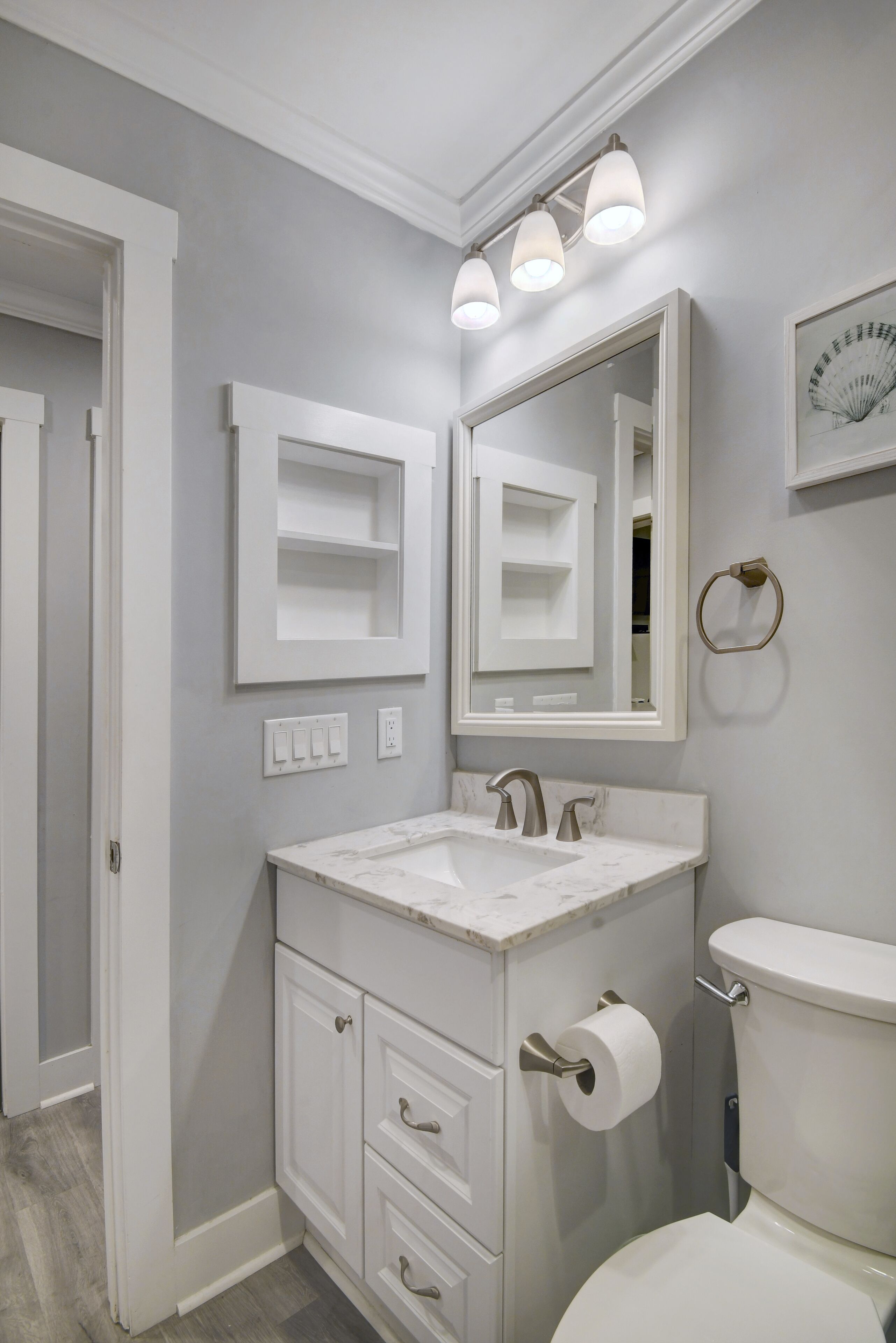 A bathroom with a white vanity, a sink, a toilet, and a mirror. There are three light fixtures above the mirror.