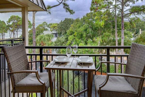 A balcony with wicker chairs and a table set for two, overlooking a lush garden and a body of water. - Awesome Ocean View! Coligny Area! Updated and CLEAN 1 Bedroom! #380 (Hilton Head Island)