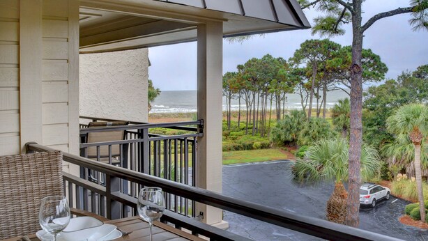A balcony with a table set for dining, overlooking a beach and a parking area with a car. - Awesome Ocean View! Coligny Area! Updated and CLEAN 1 Bedroom! #380 (Hilton Head Island)