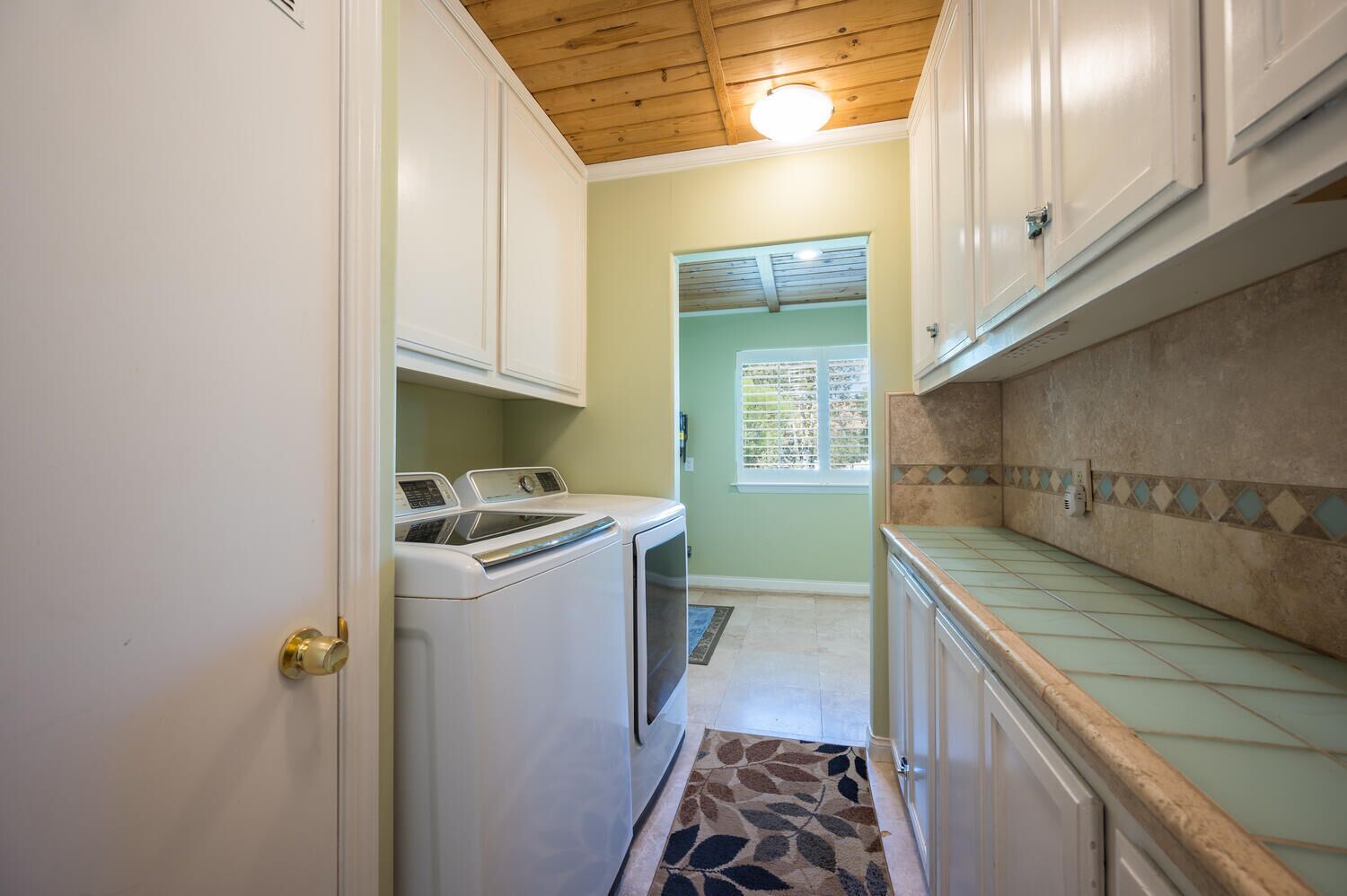 A laundry room with a washing machine and dryer, a tiled backsplash, and a wooden ceiling.