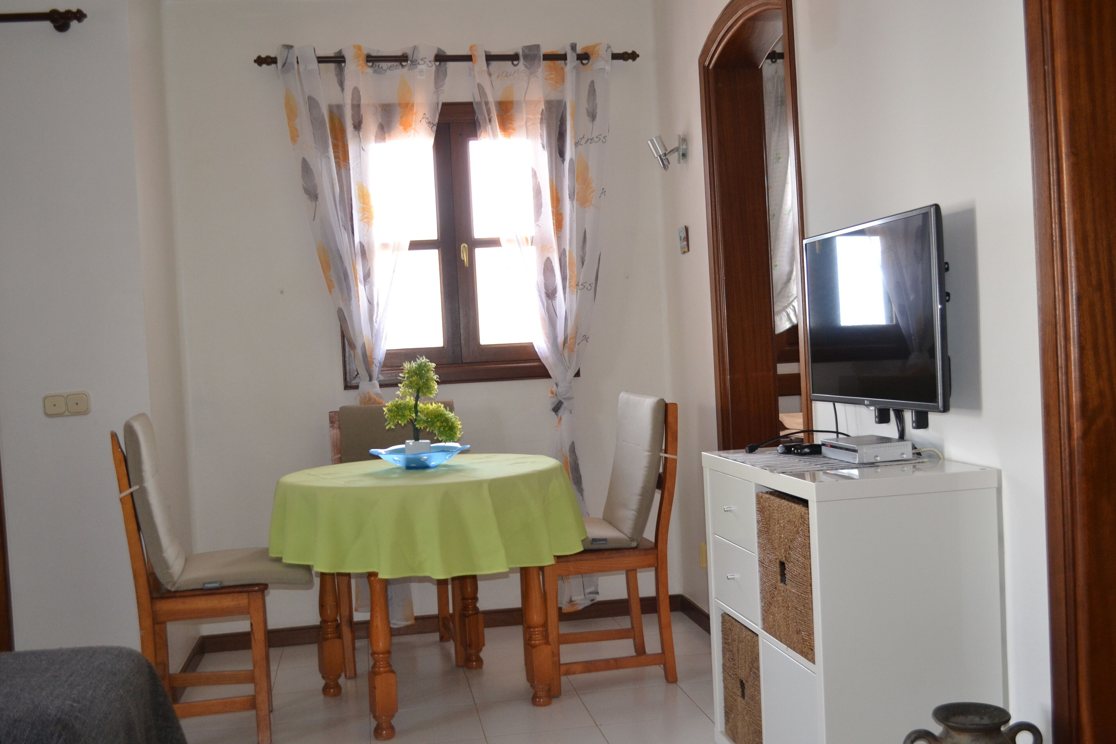 Un comedor con una mesa, sillas, un televisor y un ventanal con cortinas.