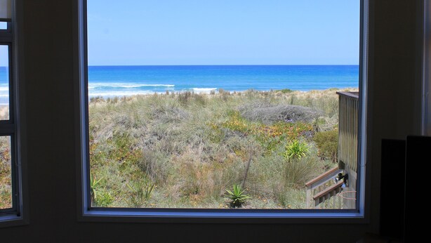 A room with a large window overlooking a beach with ocean and dunes.