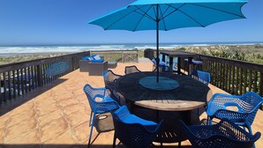 A patio with a round table and blue chairs, overlooking the ocean.