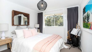 Een slaapkamer met een bed, een spiegel, een raam, een lamp en een saxofoon.
