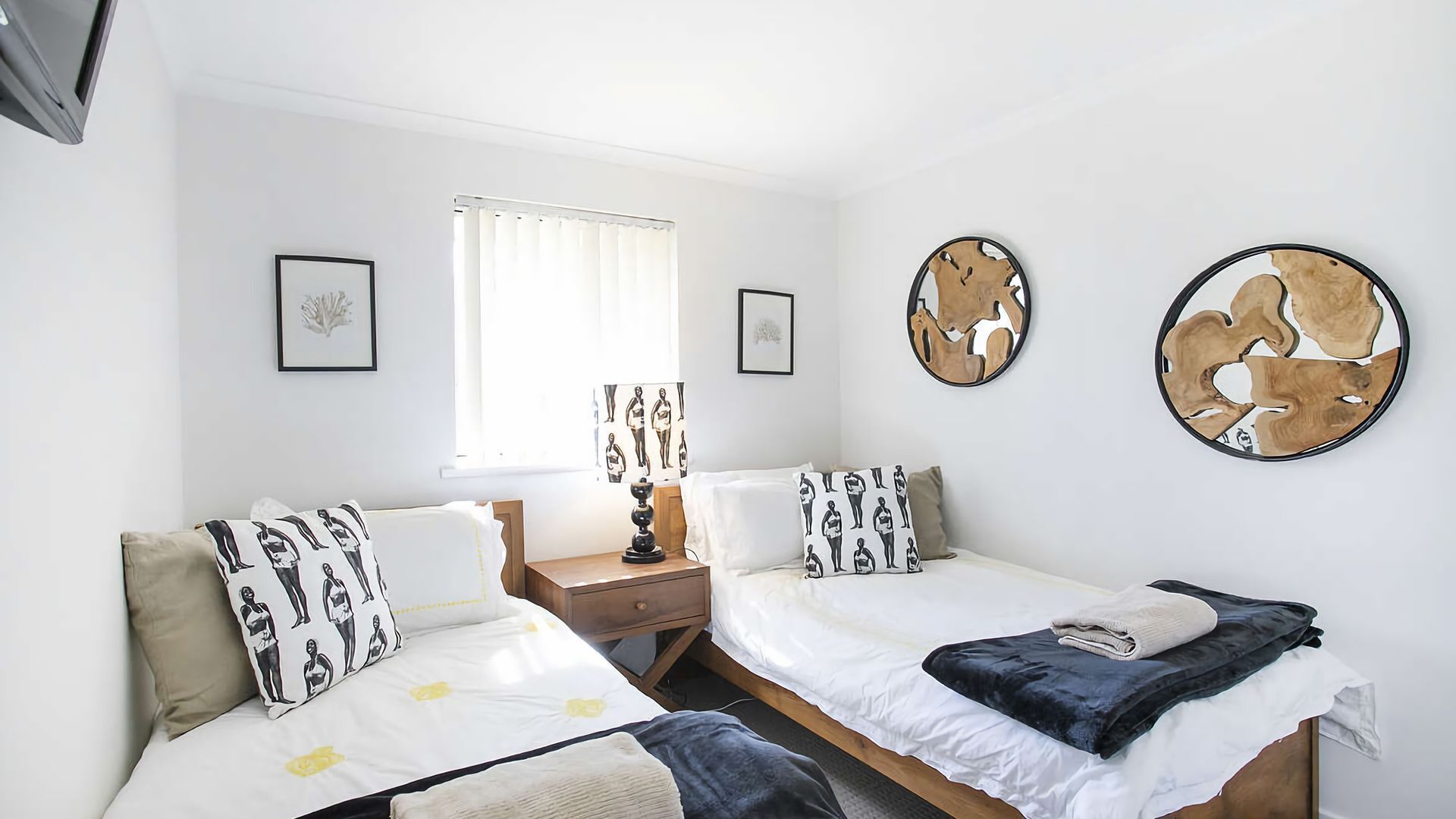 Une chambre avec deux lits, une table de chevet, une lampe et des œuvres d’art accrochées aux murs.