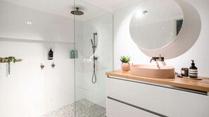 Een moderne badkamer met een glazen douchecabine, een ronde spiegel, een houten wastafelmeubel en een kleine plant in een pot.